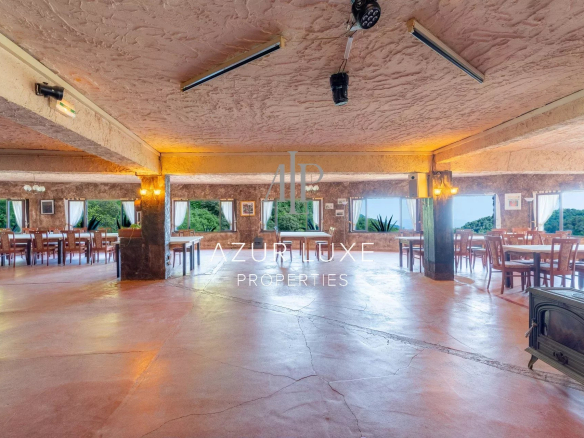 Interior of a former hotel-restaurant with tables and chairs, view of nature outside.