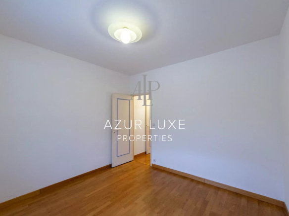 Interior of an apartment to be renovated with a wooden floor and an open door to another room.