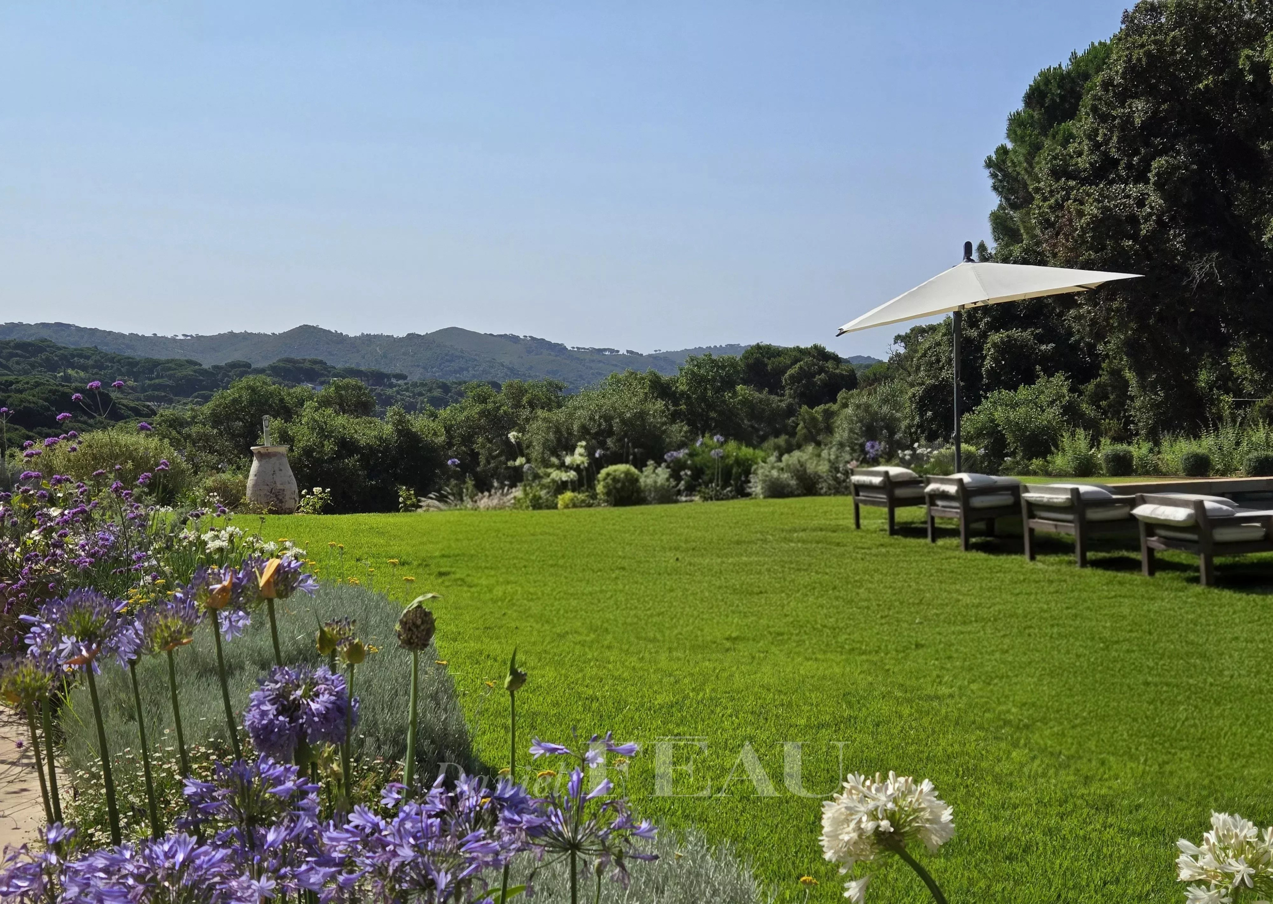 Propriété d’exception à La Croix-Valmer Vue d'un jardin avec pelouse et fleurs, parasol et chaises longues, arrière-plan naturel à La Croix-Valmer.