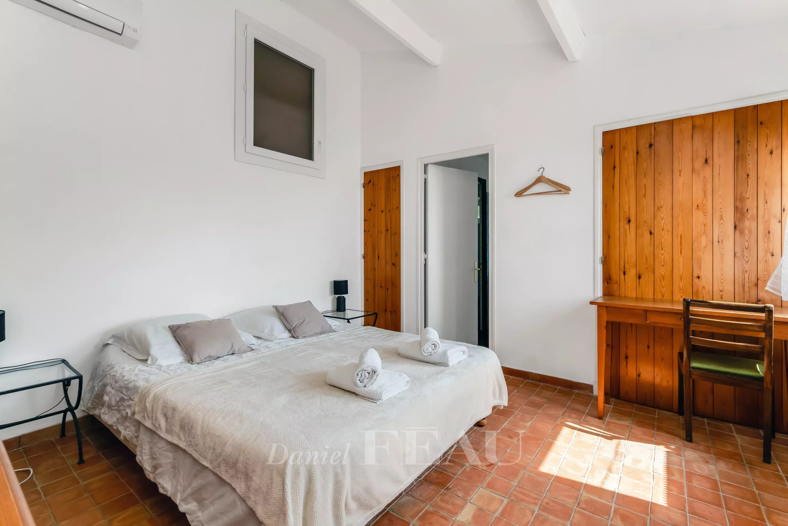 Chambre d'une villa à Rayol-Canadel, avec lit double, murs blancs et bois, bureau en bois.
