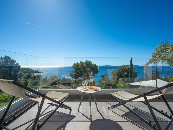 Terrasse avec vue sur la mer à Le Lavandou, deux chaises longues et une table avec des verres et une bouteille.