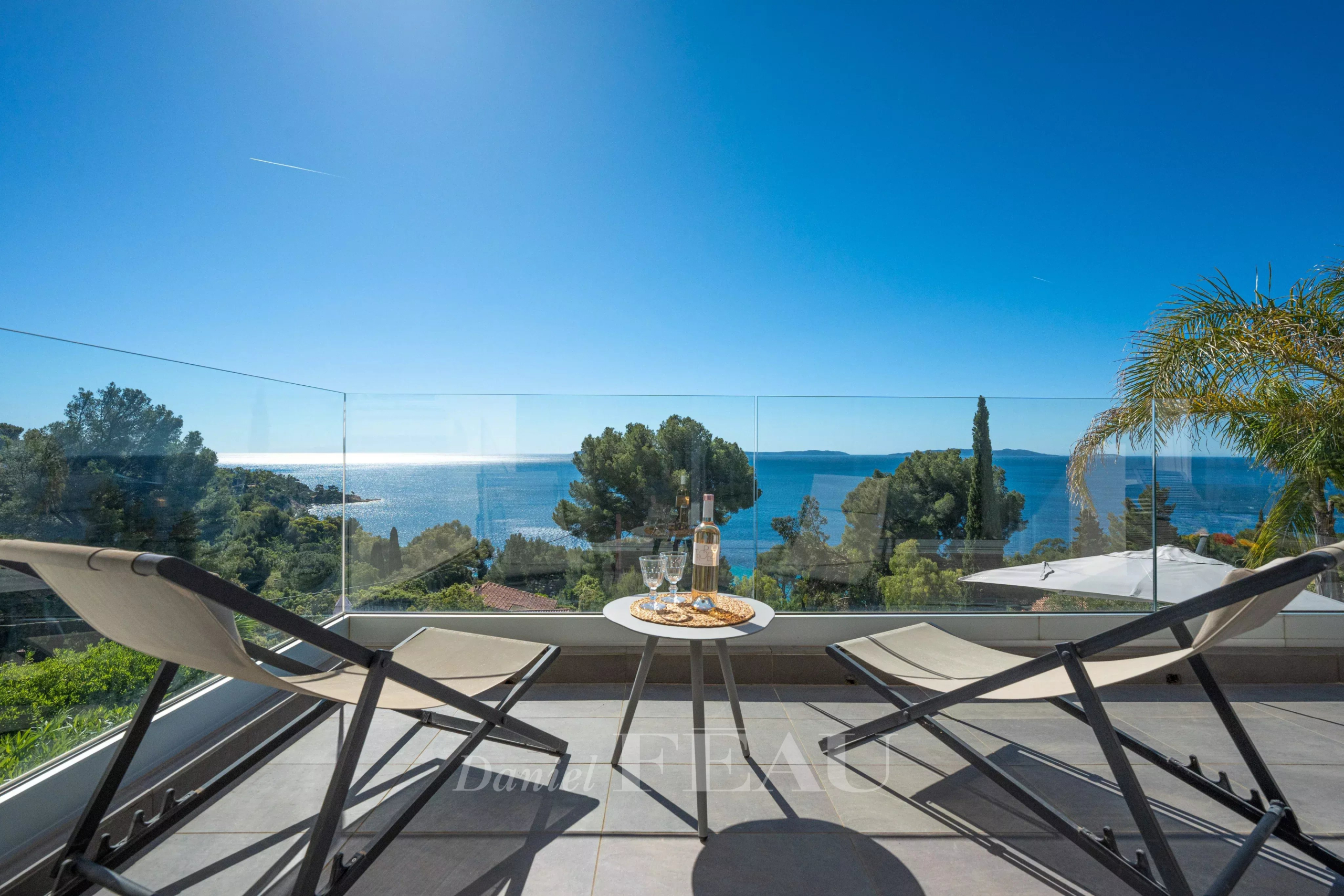 Terrasse avec vue sur la mer à Le Lavandou, deux chaises longues et une table avec des verres et une bouteille.