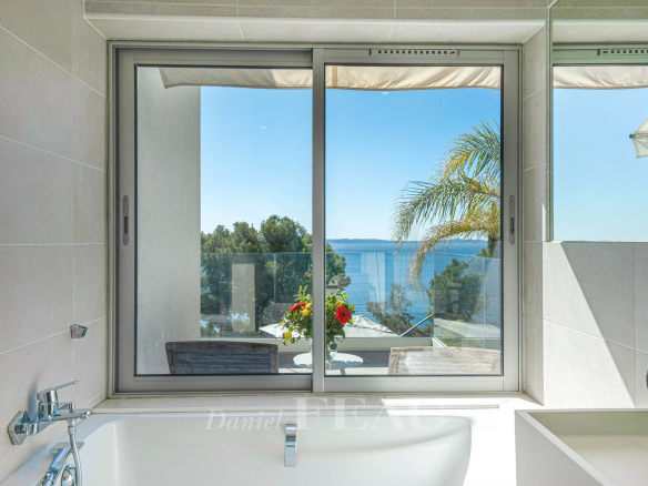 Vue depuis une fenêtre sur la mer et des arbres, avec une baignoire en premier plan.