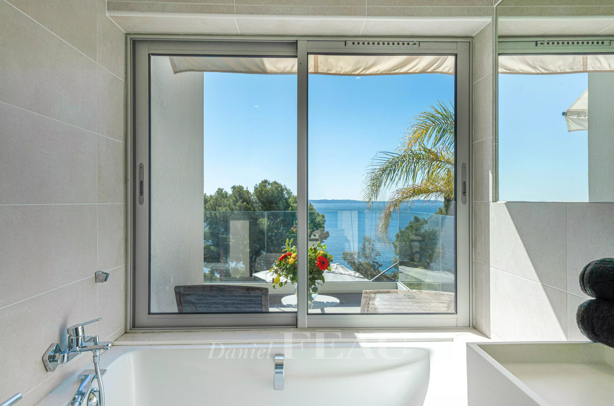 Vue depuis une fenêtre sur la mer et des arbres, avec une baignoire en premier plan.
