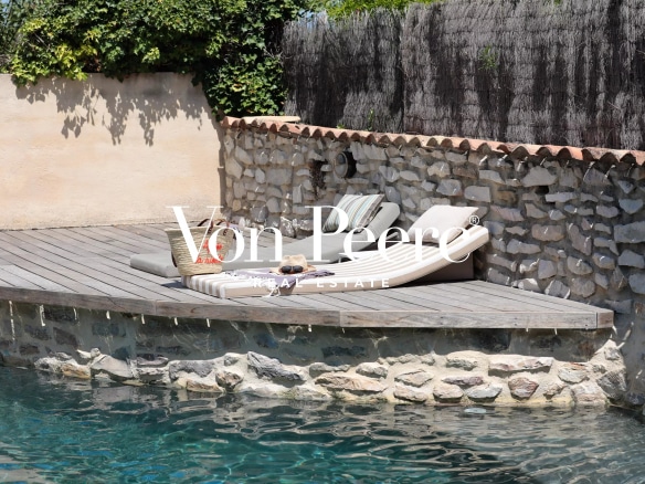 Terrasse en bois avec chaises longues au bord d'une piscine, entourée de pierres.