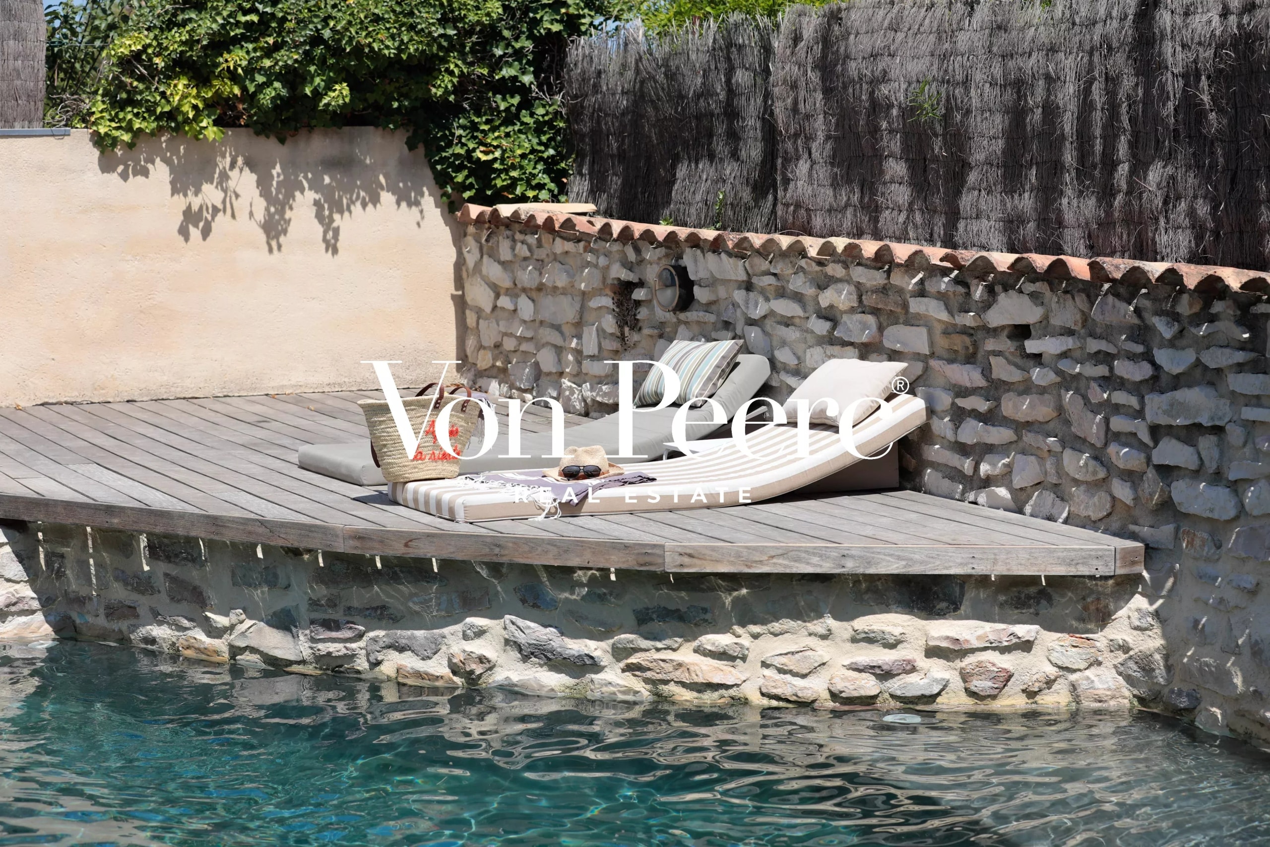 Terrasse en bois avec chaises longues au bord d'une piscine, entourée de pierres.