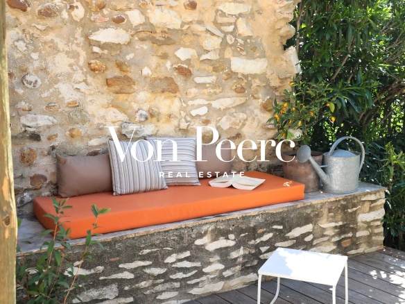 Coin détente en extérieur avec un banc en pierre et des coussins, entouré de verdure.