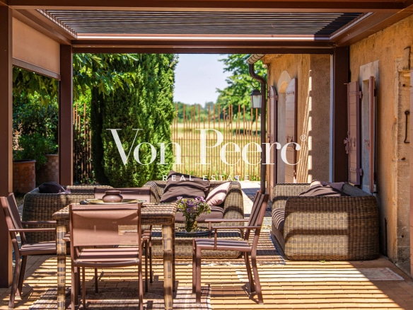 Terrasse d'un mas provençal rénové avec mobilier en osier et vue sur un parc.