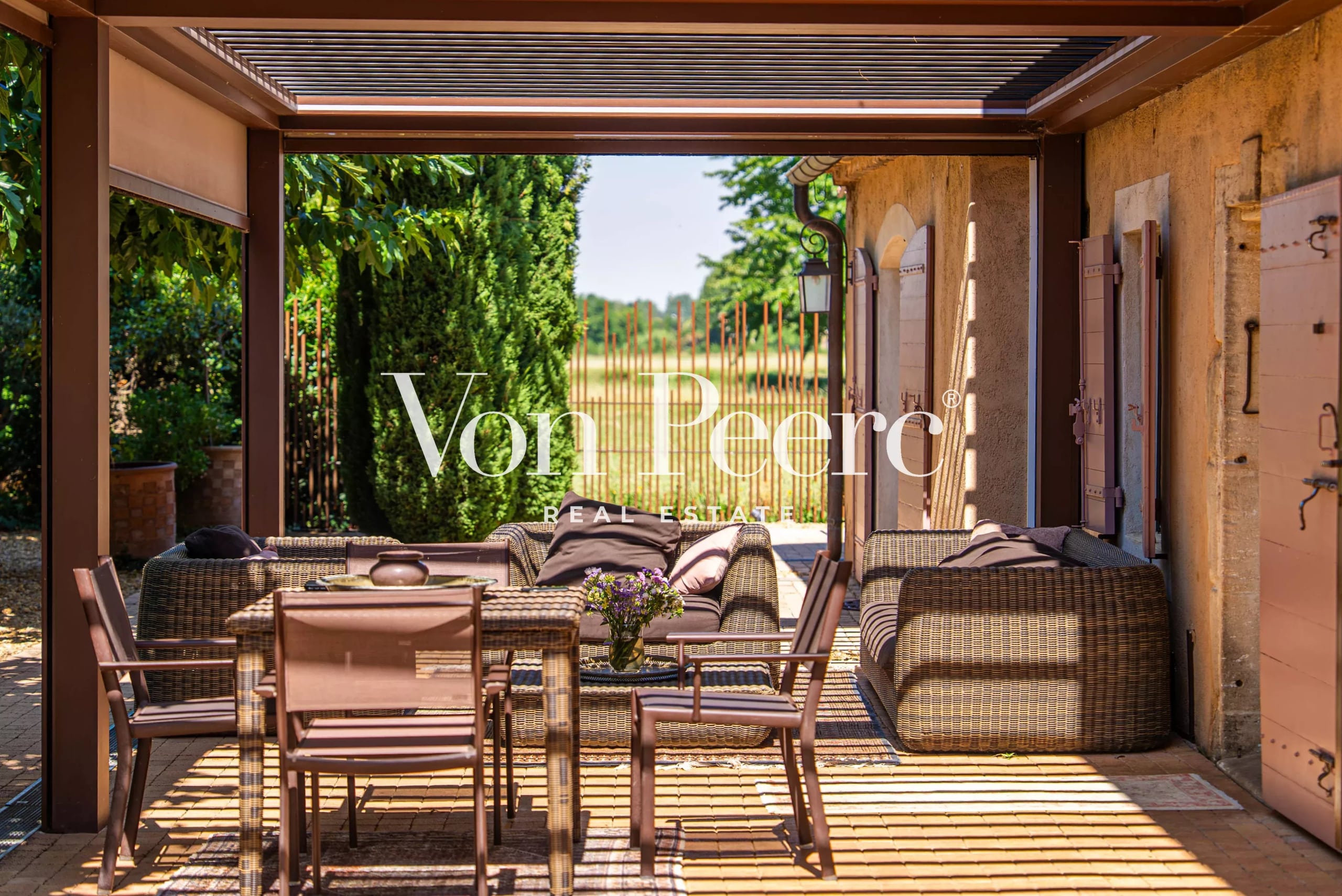 Terrasse d'un mas provençal rénové avec mobilier en osier et vue sur un parc.