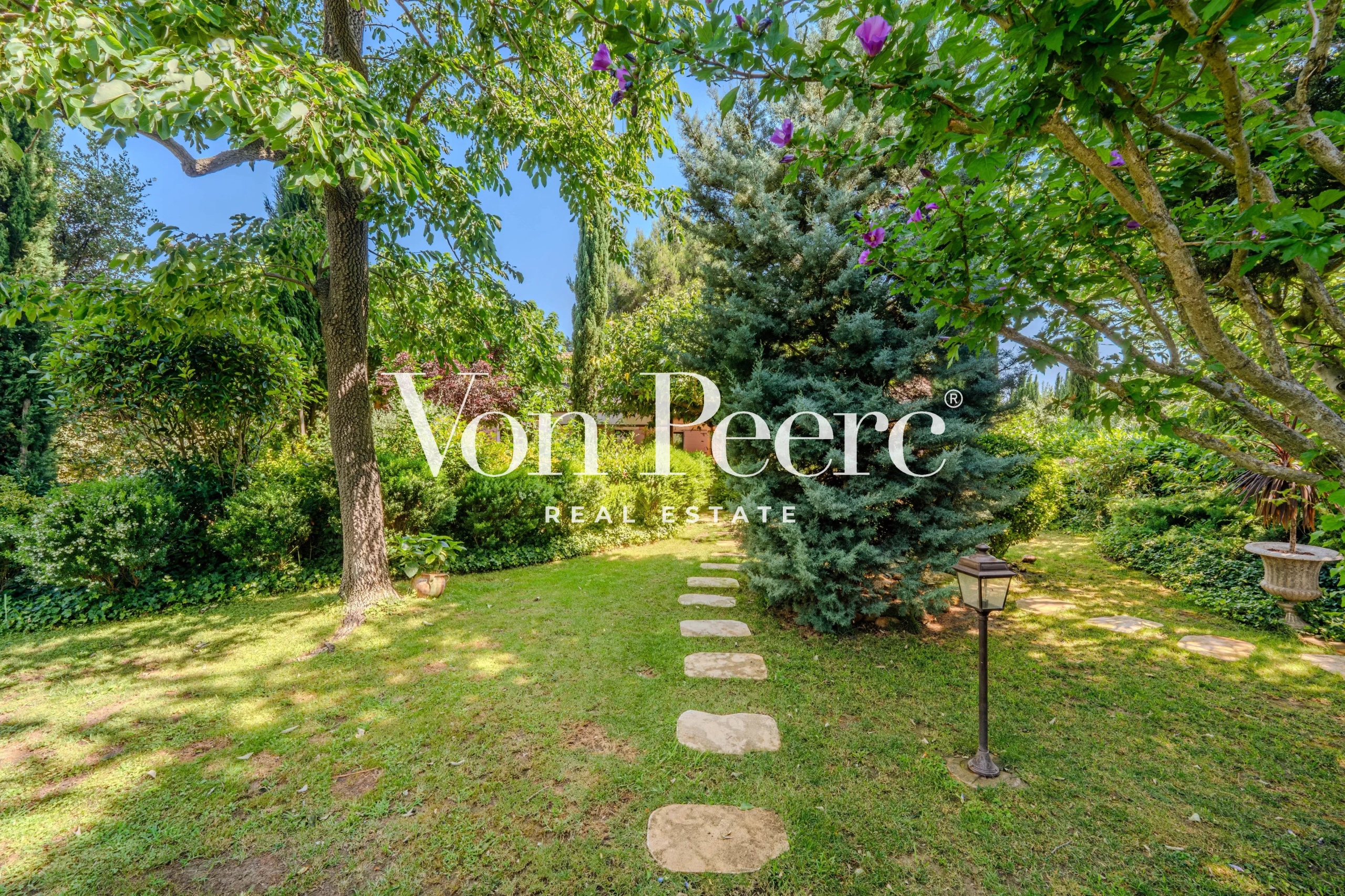 Jardin d'un mas provençal avec allée en pierre et végétation luxuriante, près d'Arles.