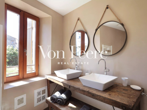 Salle de bain moderne avec deux lavabos sur un meuble en bois et fenêtres ouvertes sur un jardin.