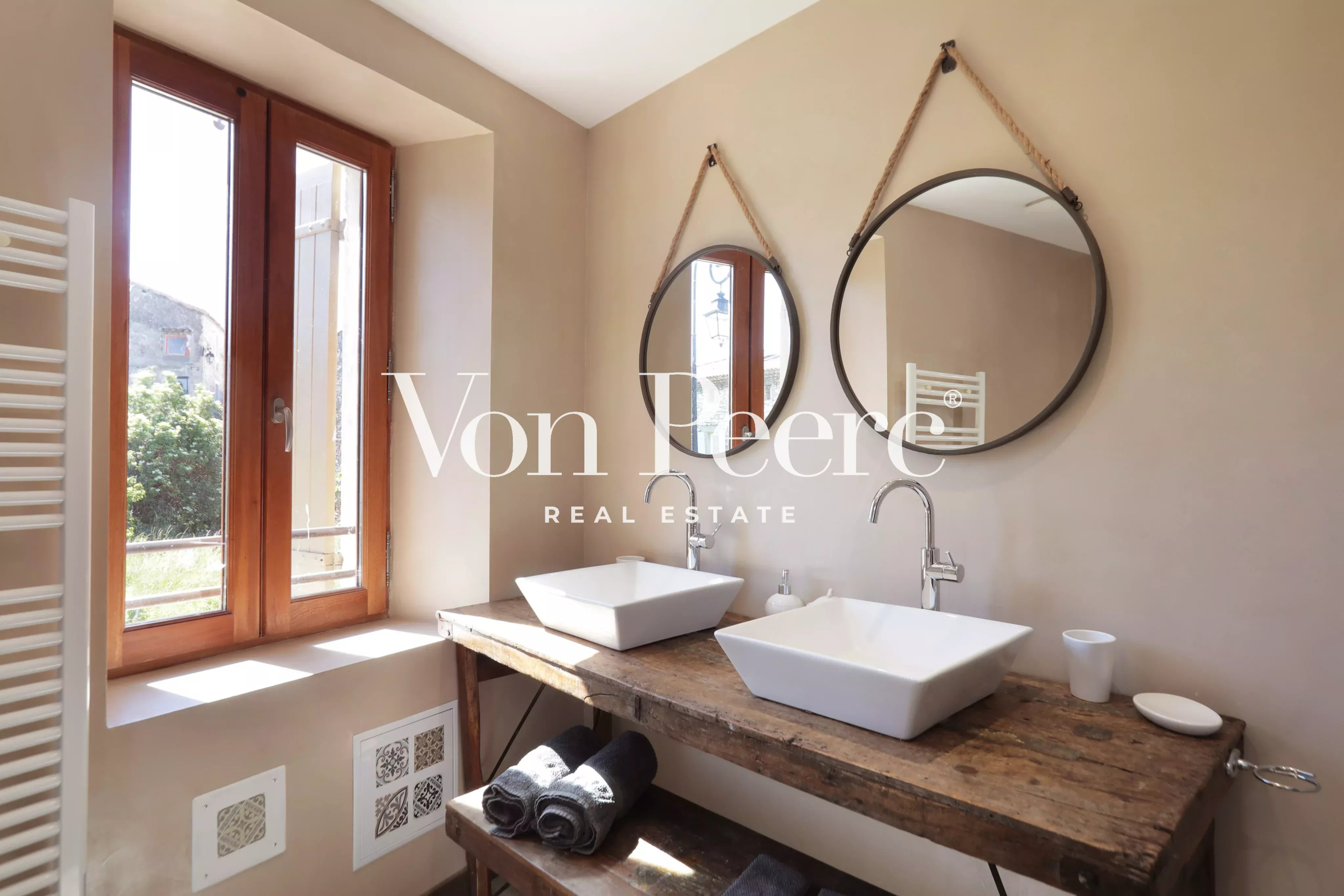 Salle de bain moderne avec deux lavabos sur un meuble en bois et fenêtres ouvertes sur un jardin.