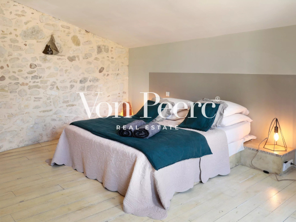 Chambre d'une maison de caractère avec murs en pierre et lit double, décorée avec des éléments modernes.
