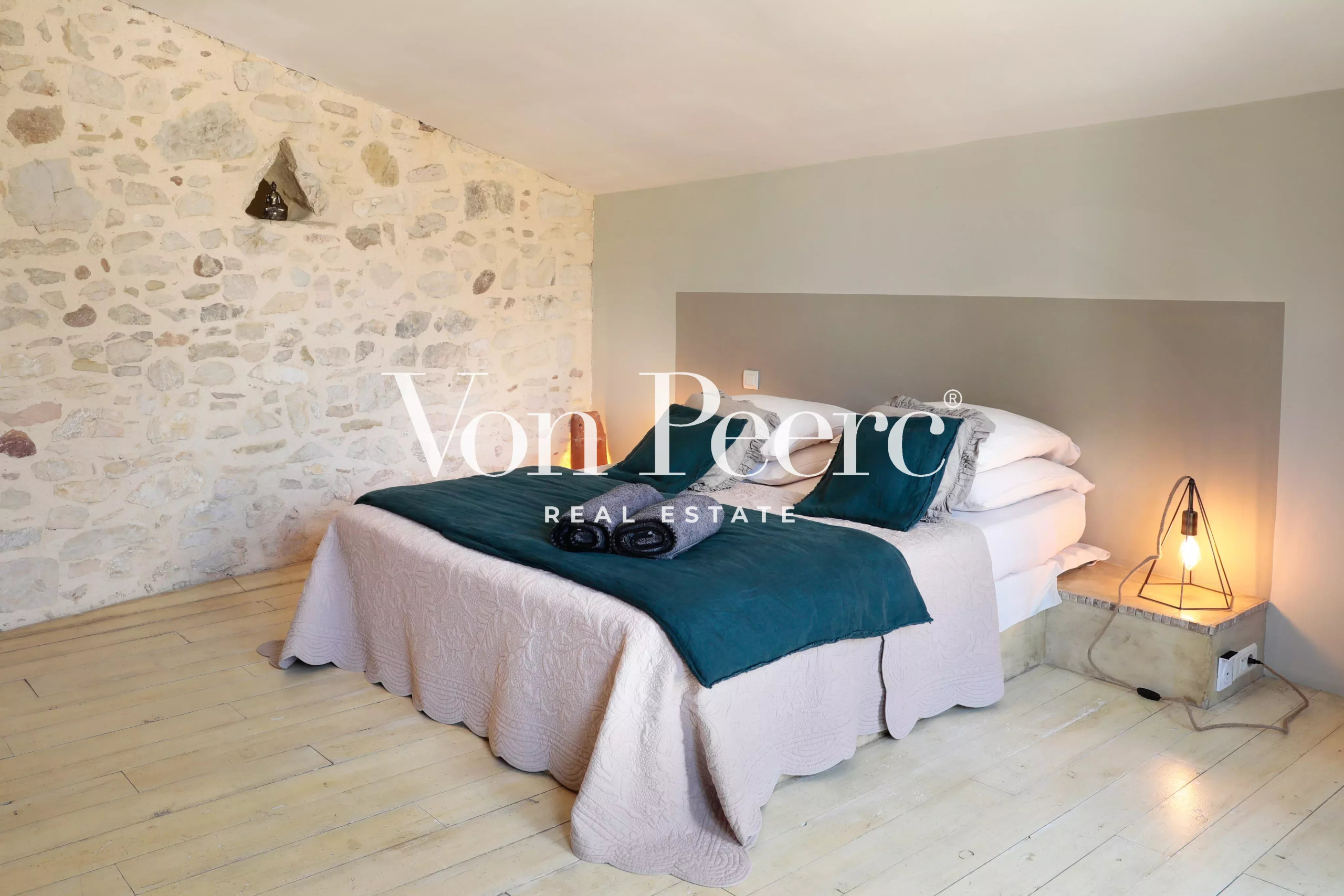 Chambre d'une maison de caractère avec murs en pierre et lit double, décorée avec des éléments modernes.