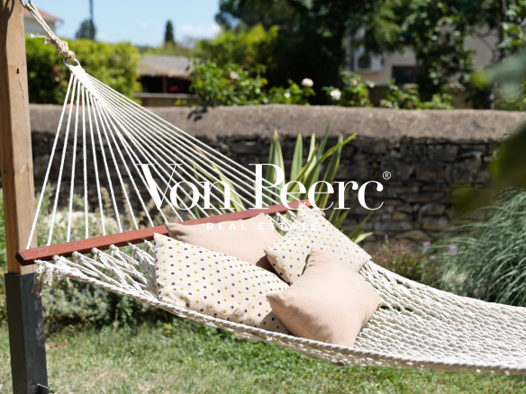 Hamac avec coussins dans un jardin, maison de caractère en arrière-plan.