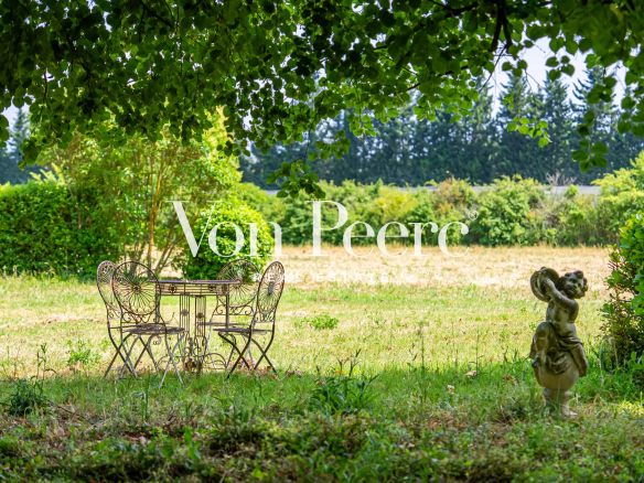 Table et chaises en fer forgé dans un jardin verdoyant avec des arbres en arrière-plan.