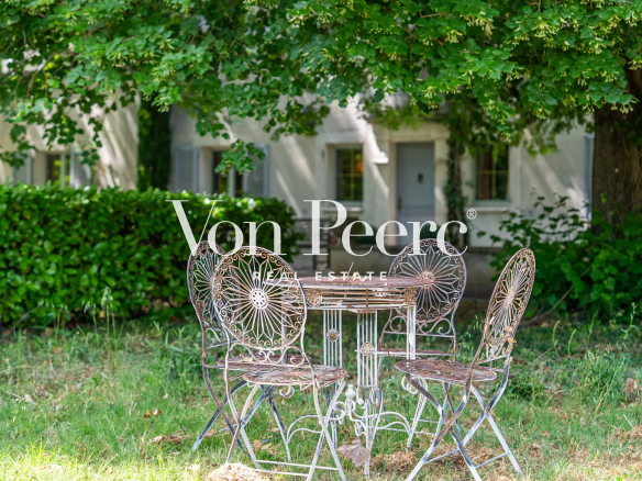 Table et chaises en fer forgé sous un arbre dans un jardin verdoyant d'une propriété près d'Avignon.