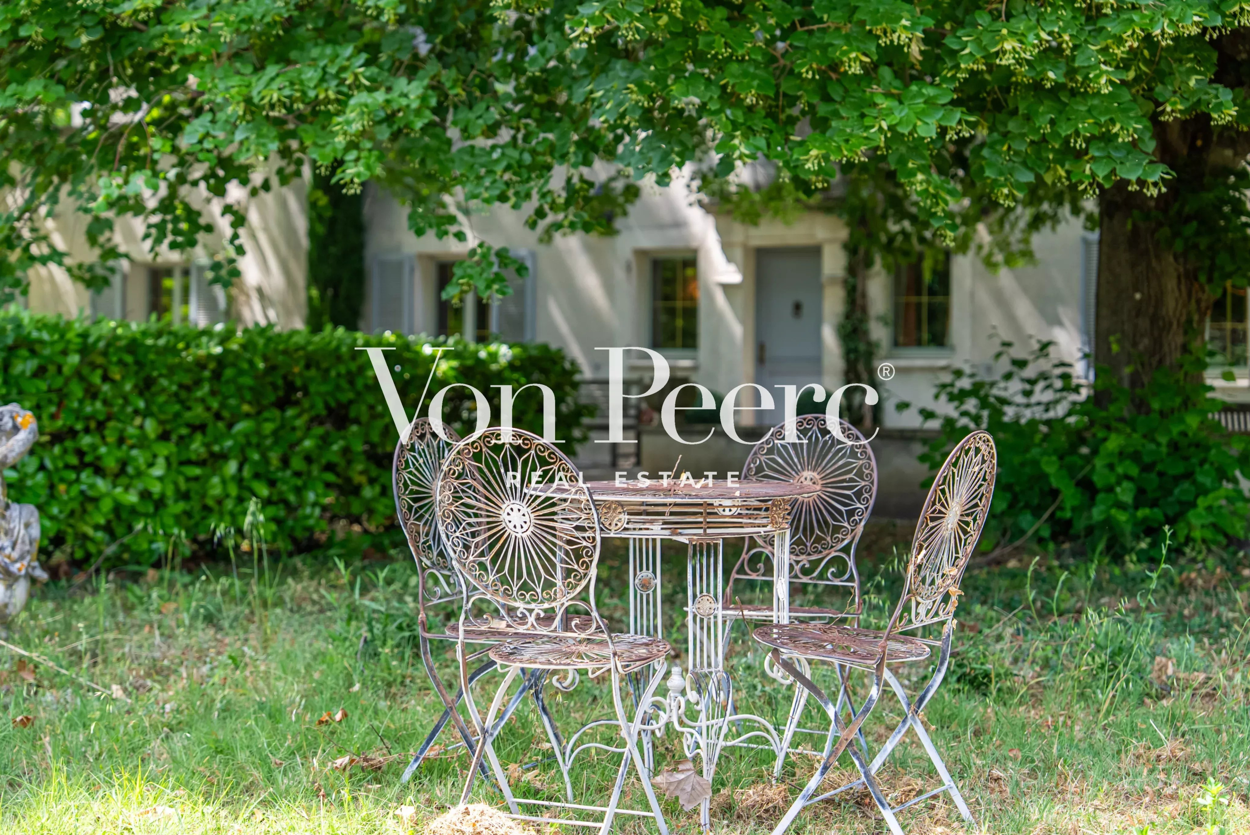 Table et chaises en fer forgé sous un arbre dans un jardin verdoyant d'une propriété près d'Avignon.