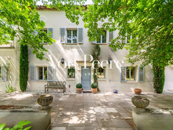 Mas provençal entouré d'arbres et de verdure, avec une cour en pierre.