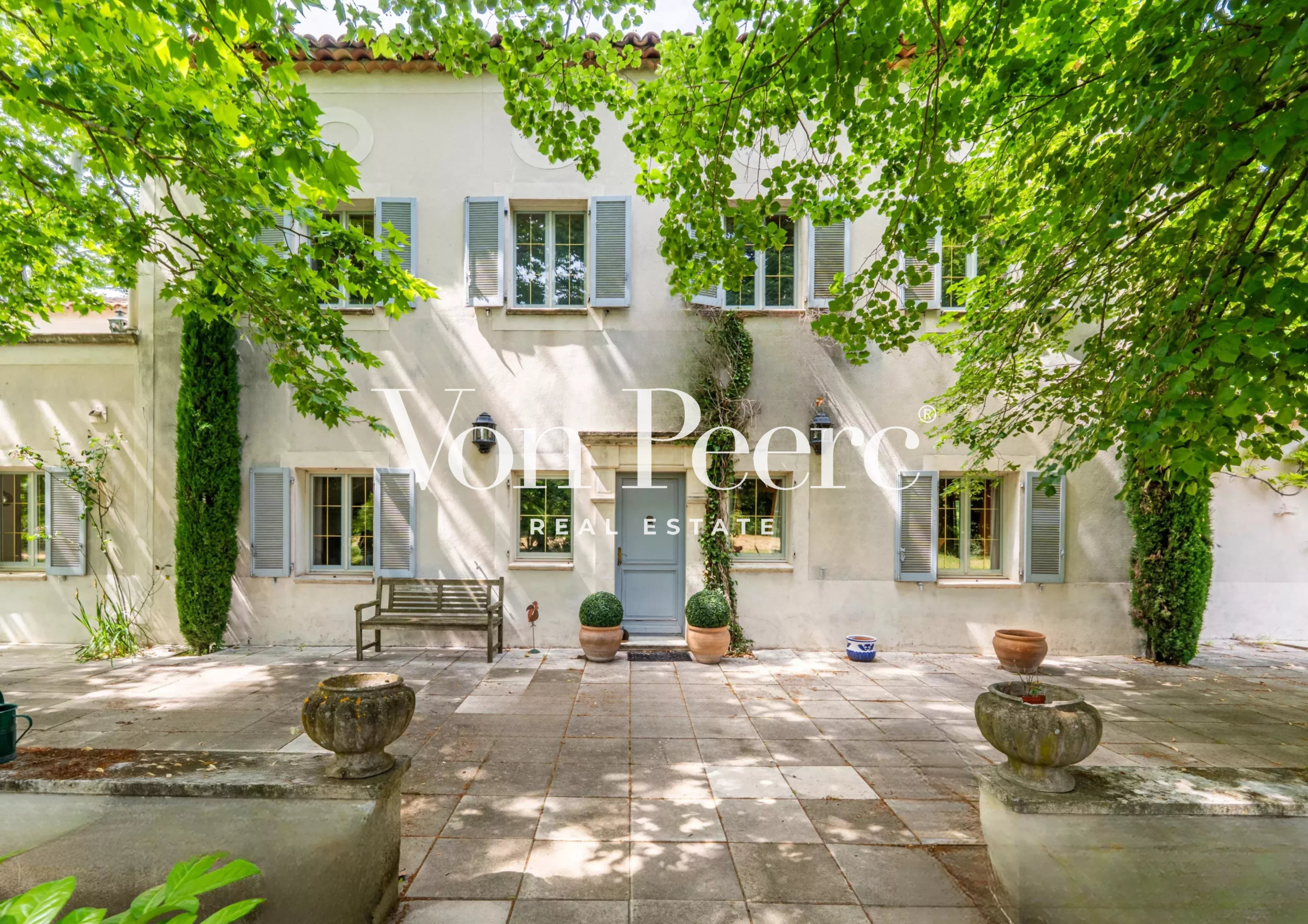 Mas provençal entouré d'arbres et de verdure, avec une cour en pierre.