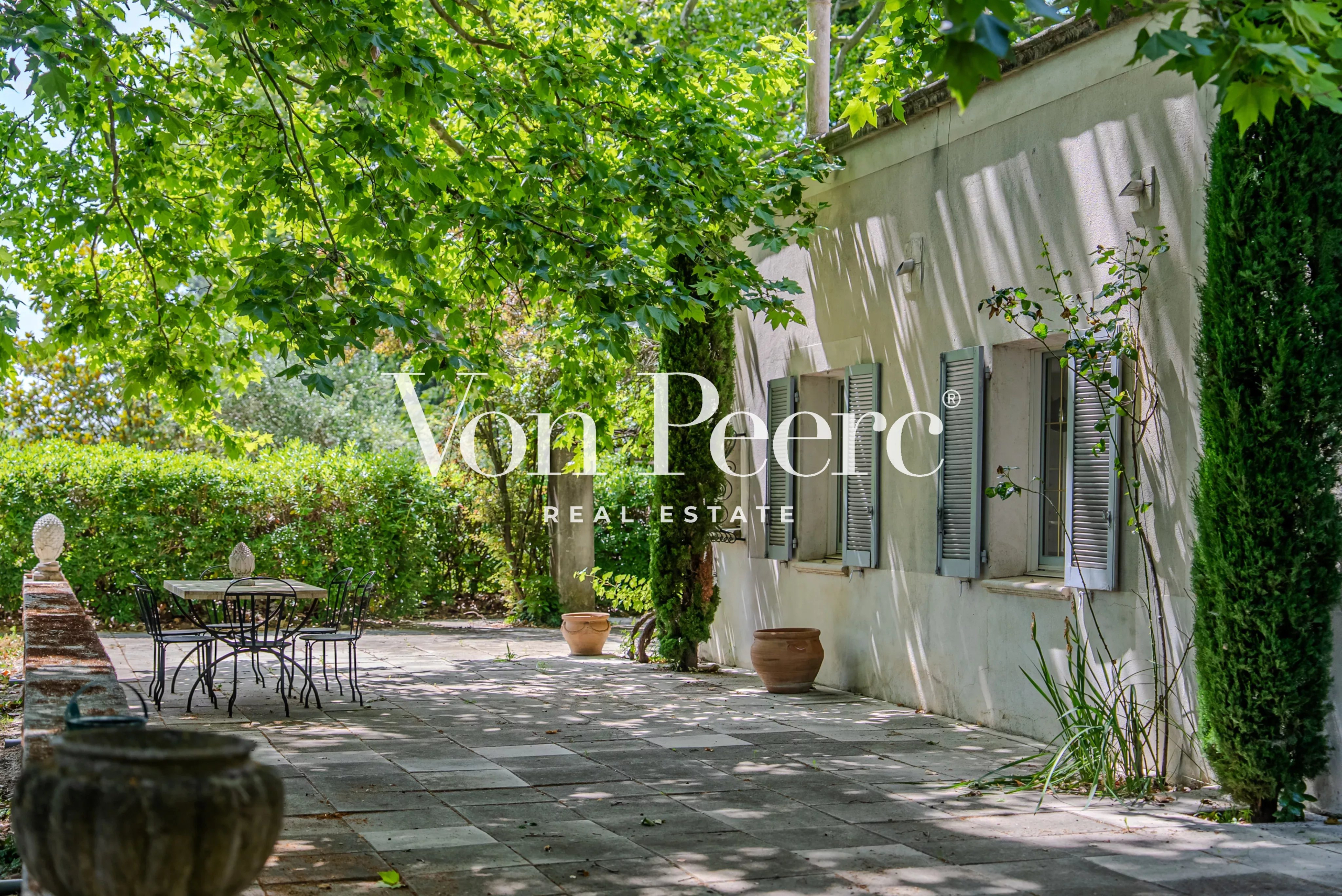 Terrasse ombragée d'une propriété provençale avec des plantes et des pots, en pleine verdure.