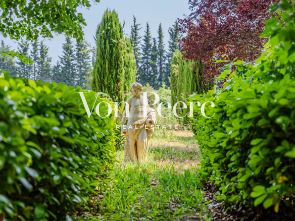 Jardin verdoyant avec une statue au centre, entouré d'arbustes et d'arbres.
