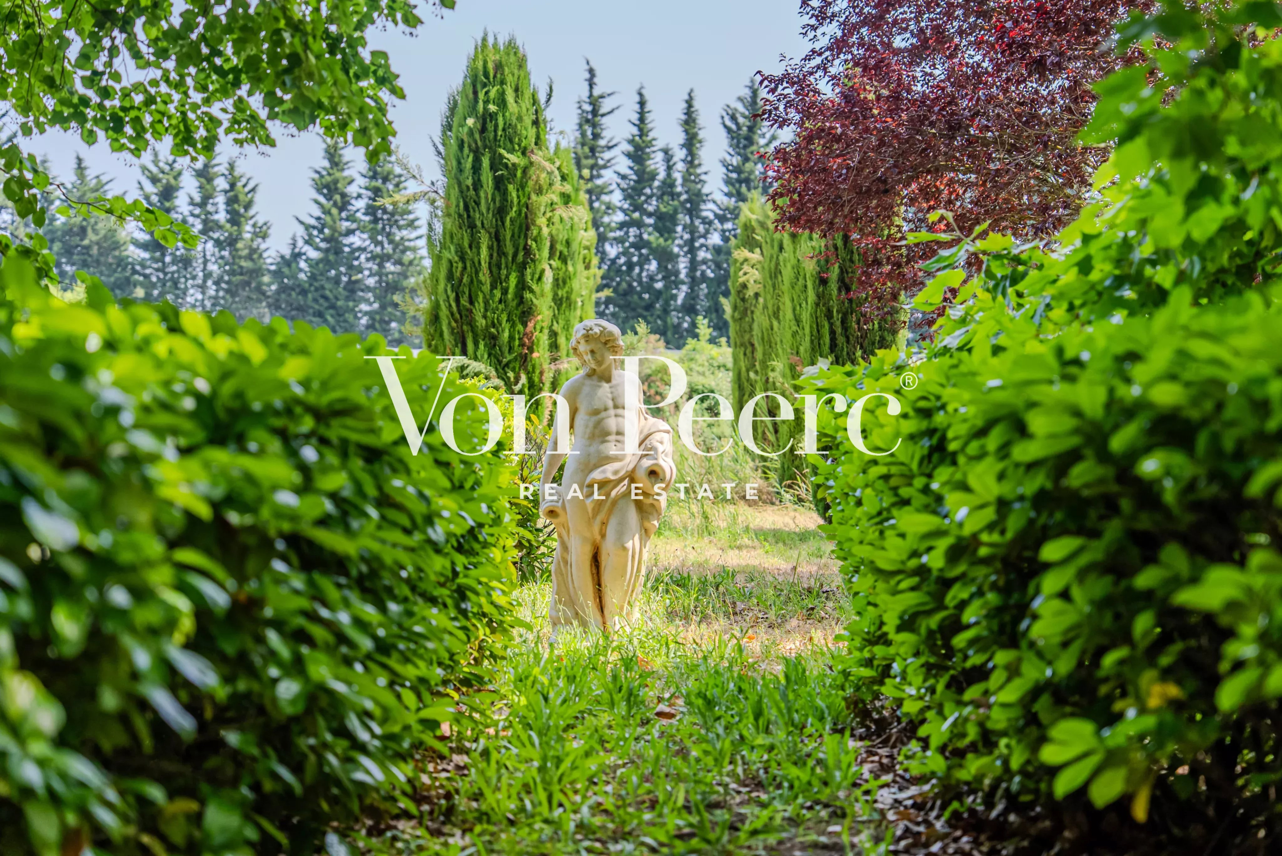 Jardin verdoyant avec une statue au centre, entouré d'arbustes et d'arbres.