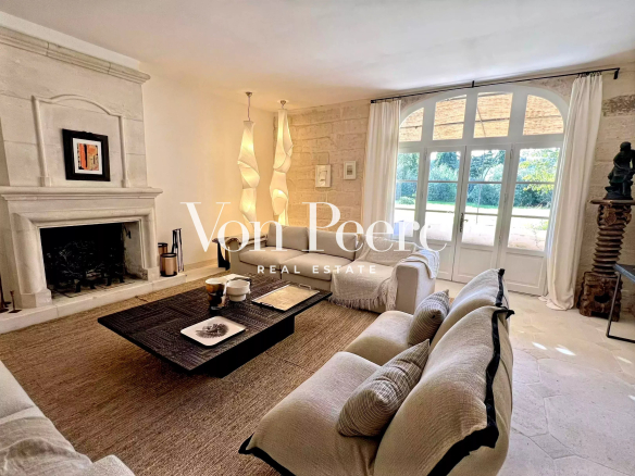 Intérieur d'une maison ancienne rénovée avec un salon lumineux, cheminée et accès au jardin.
