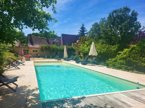 Swimming pool surrounded by greenery with a stone house in the background, Les Eyzies.