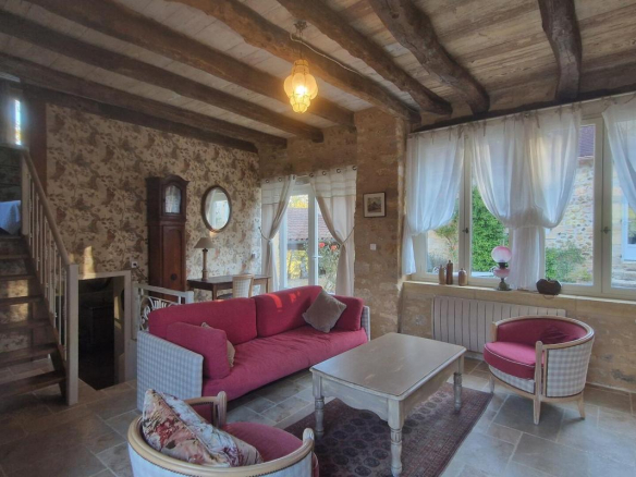 Intérieur d'une maison en pierre avec salon confortable, fenêtres lumineuses et mobilier classique.