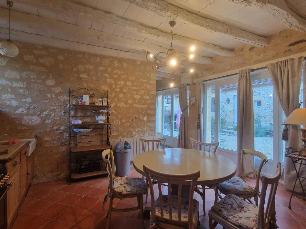 Cuisine d’une propriété aux Eyzies Intérieur d'une cuisine rustique avec une table ronde et des chaises, fenêtres donnant sur l'extérieur.