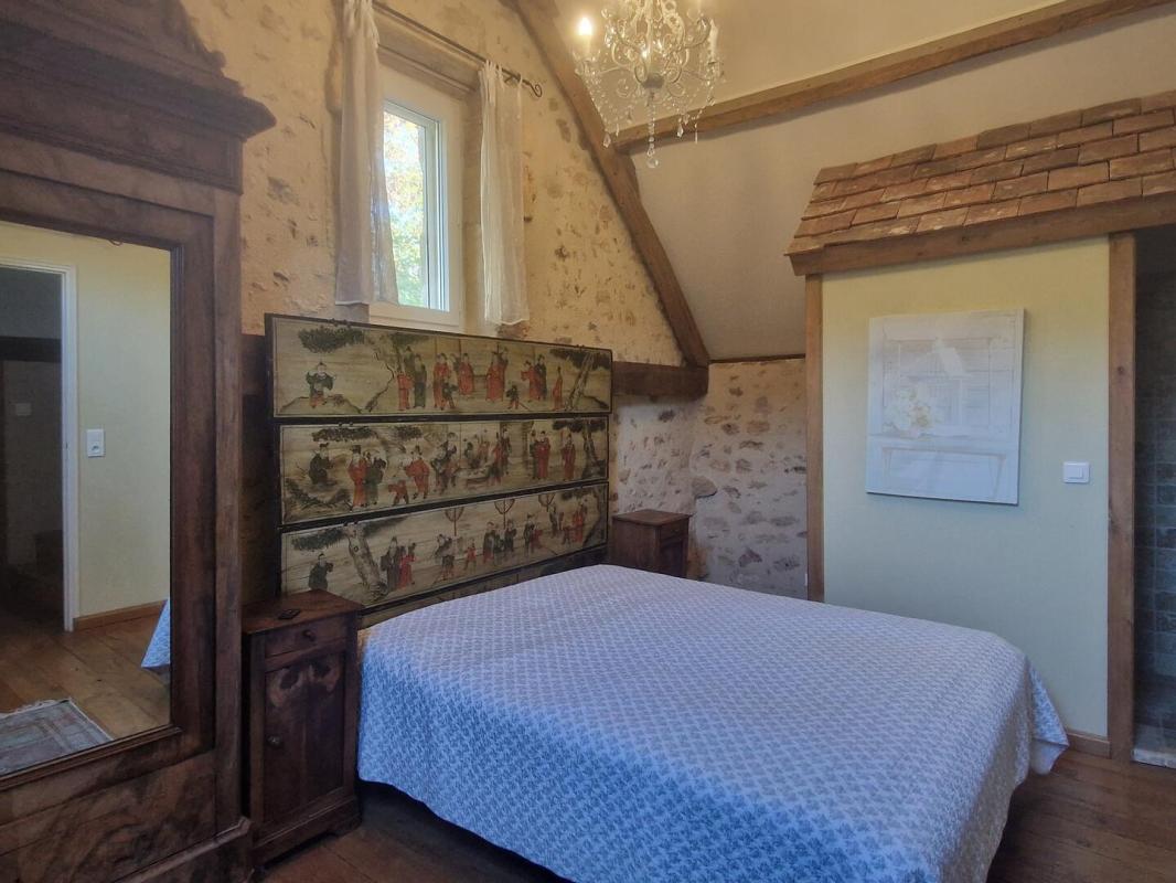 Chambre de propriété aux Eyzies Chambre d'une propriété en pierres avec un lit double, miroir et décoration murale.