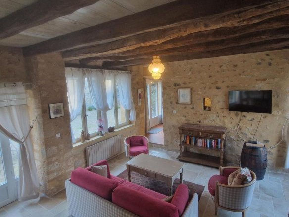 Intérieur d'une maison en pierre avec salon confortable, meubles clairs et poutres apparentes.