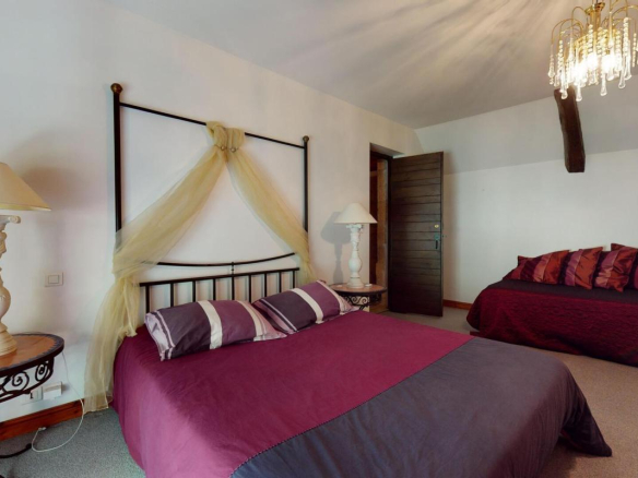 Chambre d'une demeure en pierres avec lit double et lit simple, décorée avec des coussins colorés.