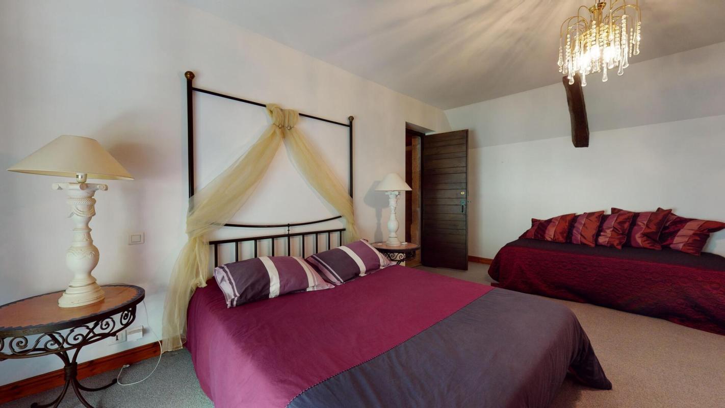 Chambre d'une demeure en pierres avec lit double et lit simple, décorée avec des coussins colorés.