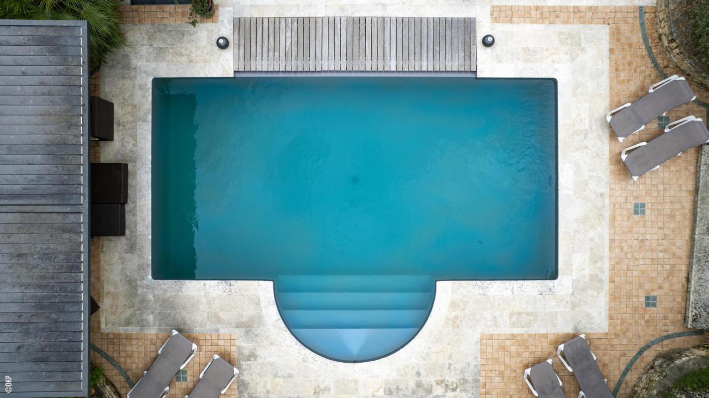 Vue aérienne d'une piscine avec terrasse, entourée de chaises longues.