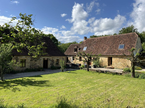 Stone farmhouse with main house, barn and guest house on green grounds.