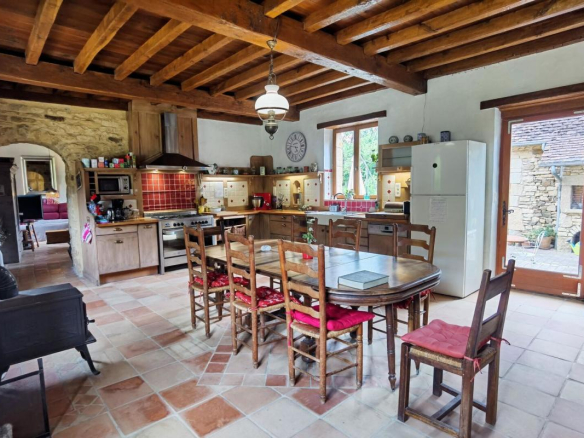 Interior of a rustic kitchen with a wooden table and chairs, stone walls and exposed beams.
