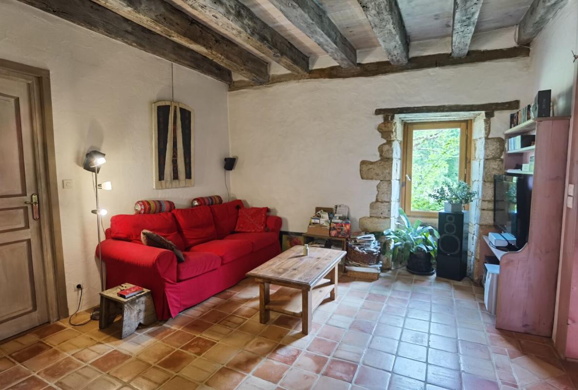 Living room of a farmhouse in Excideuil Interior of a living room with a red sofa, stone walls and exposed beams.
