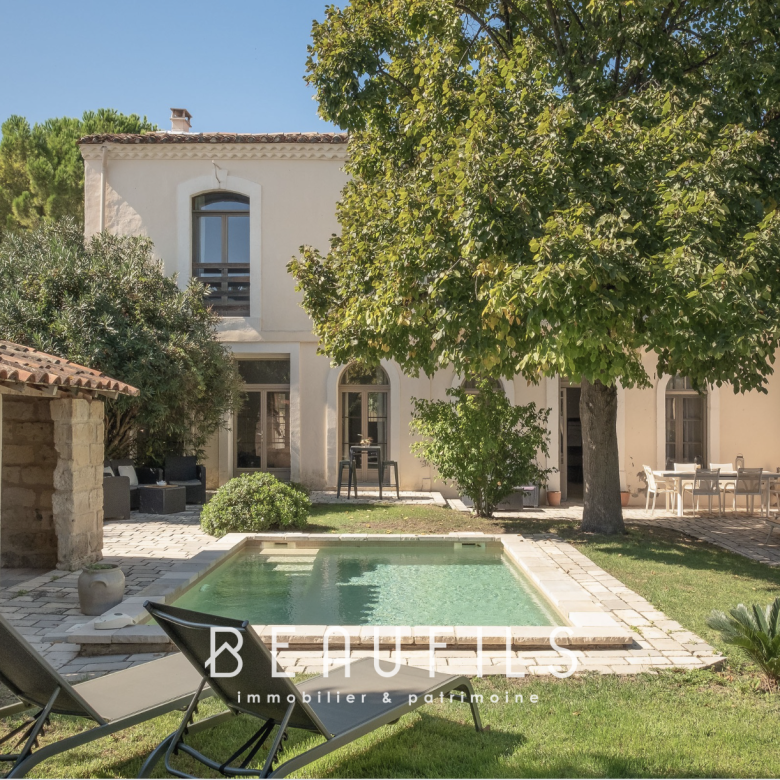 Rear courtyard of a Mediterranean-style house with a rectangular pool, stone patio, and lush trees.