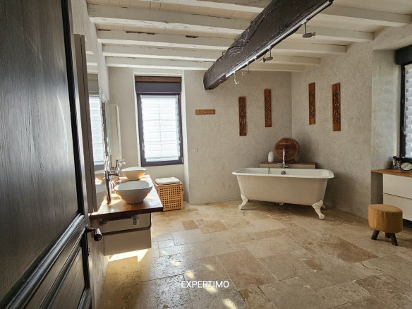 Rustic bathroom with a freestanding clawfoot tub, wooden beams, and a double sink vanity under large windows.