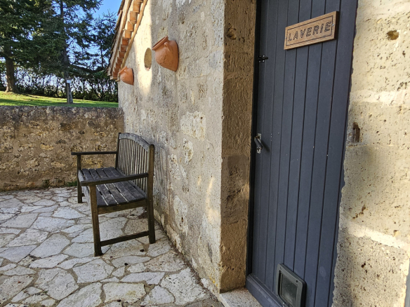 Blue door labeled 'LAVERIE' set in a rustic stone wall, with a wooden bench and stone courtyard in bright sunlight