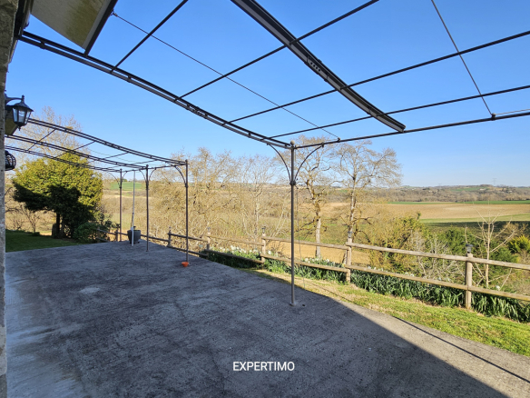 Outdoor concrete patio under a metal pergola frame with a scenic countryside view and a wooden railing beyond; clear blue sky.