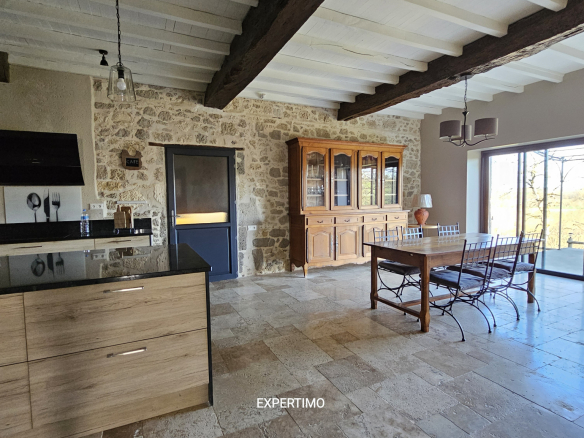 Rustic kitchen-dining area with exposed stone wall, wooden beams, and large glass doors opening to an outdoor view.