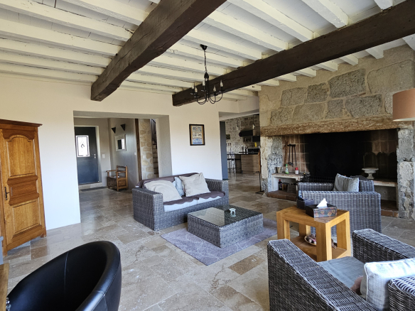 Rustic living room with a large stone fireplace, whitewashed ceiling beams, and wicker seating around a glass coffee table.