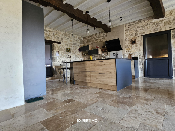 Rustic kitchen with stone walls, exposed wooden beams, and a central wooden island with bar stools.