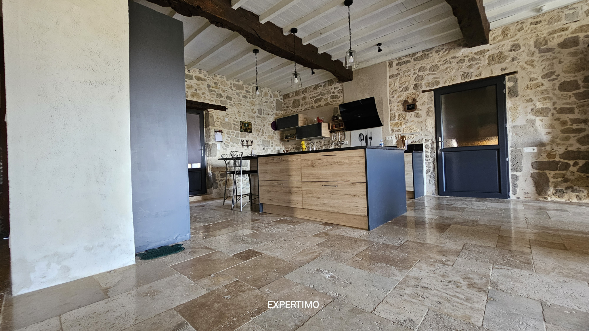 Rustic kitchen with stone walls, exposed wooden beams, and a central wooden island with bar stools.