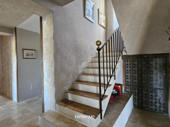 Stone-walled interior with a concrete staircase and black metal railing, and framed paintings on the wall above the stairs.