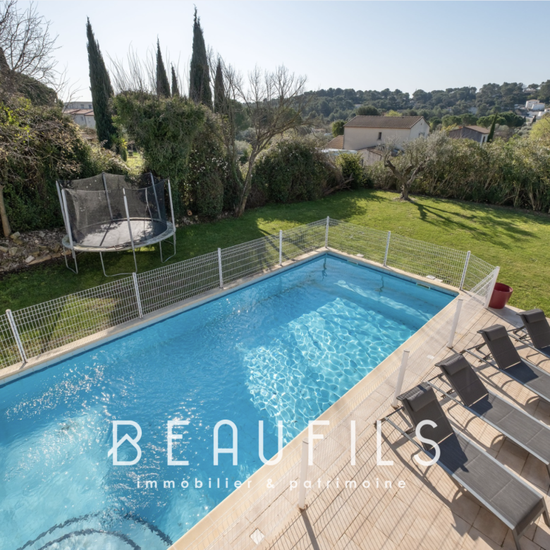 Backyard with a rectangular pool, safety fence, tiled deck, six lounge chairs, and a trampoline on the lawn; trees in the background.
