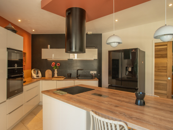 Modern kitchen with white cabinetry, wood island, black backsplash, and orange accent wall; pendant lights overhead.